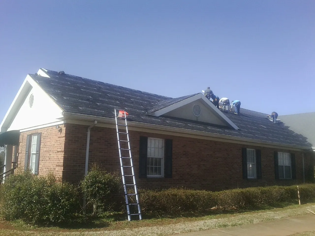 Crew tearing shingles off a brick ranch roof with a ladder set — Emergency Roof Repair work by our crew in Catharpin