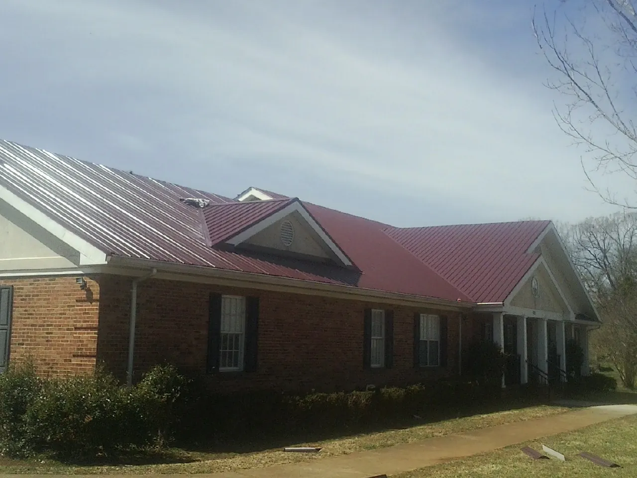 Red metal roof with gabled entries on a long brick building, from a Hail Damage Roof Repair job in Catharpin