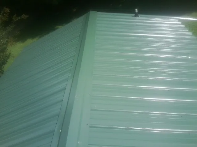 New green metal panels meeting at the ridge of a roof — Flat Roof Repair work by our crew in Catharpin