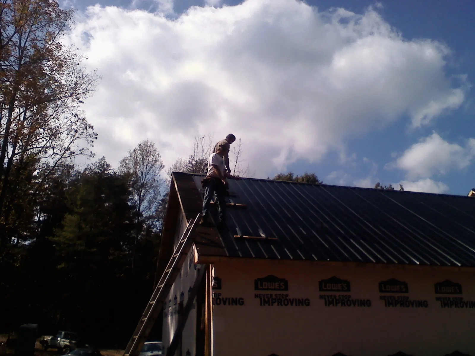 Roofer fastening dark metal panels high against a cloudy sky, from a Roof Inspection job in Catharpin