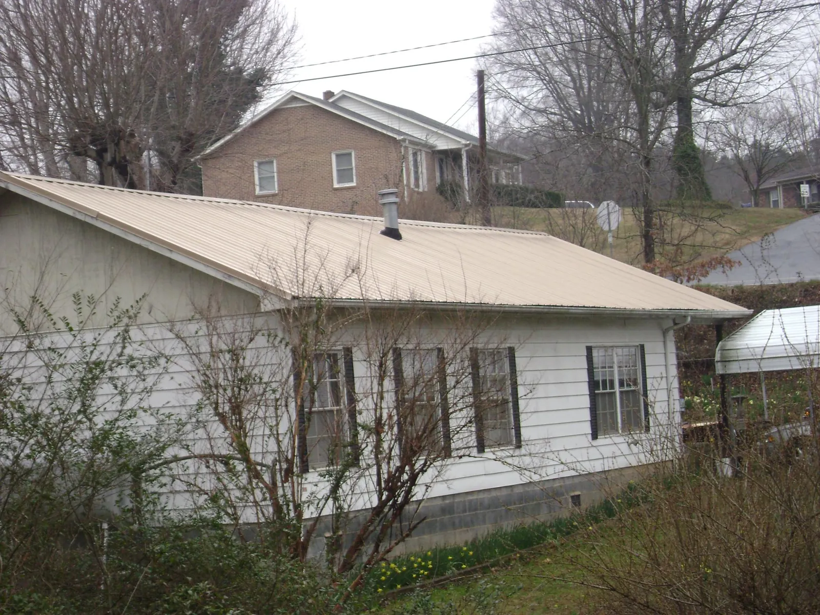 Tan metal roof on a white sided house set into a hillside — Commercial Roofing by Roofing Brothers in Catharpin